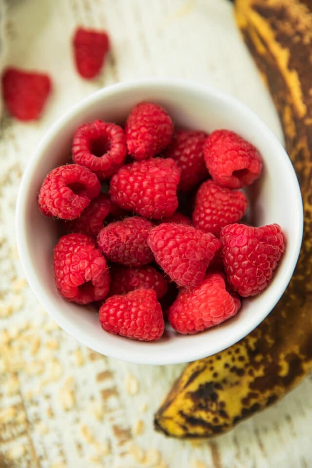 overhead view of raspberries in a white bowl and a ripe banana on the side
