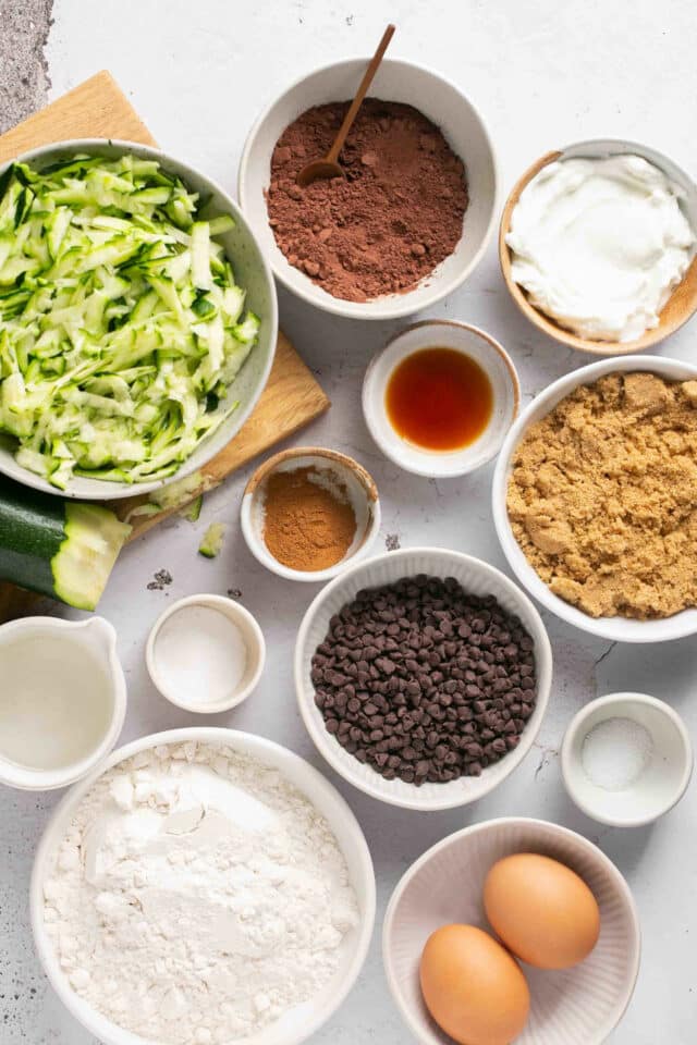 Shredded zucchini, eggs, cocoa powder, flour, sugar and other ingredients divided into small bowls.