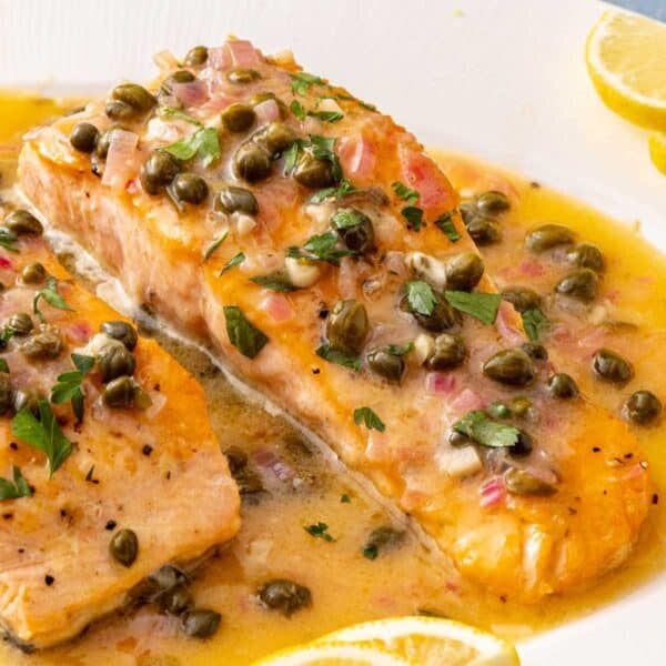 Salmon Piccata on a white plate served with lemon wedges.