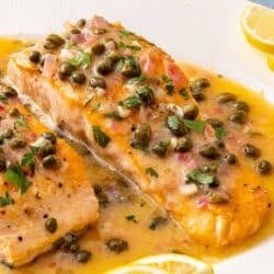 Salmon Piccata on a white plate served with lemon wedges.