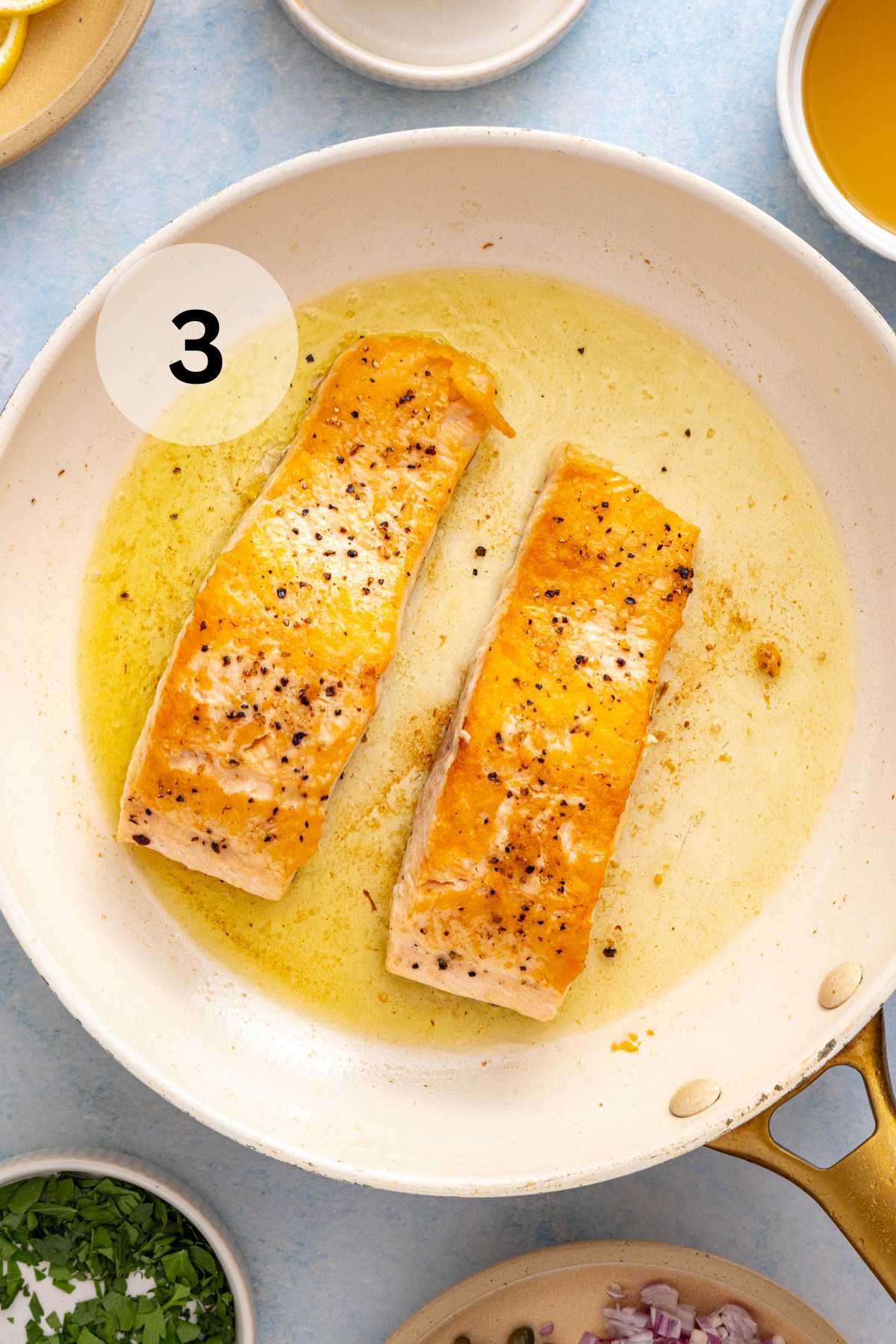 Salmon fillets cooking skin side down in a skillet with oil.