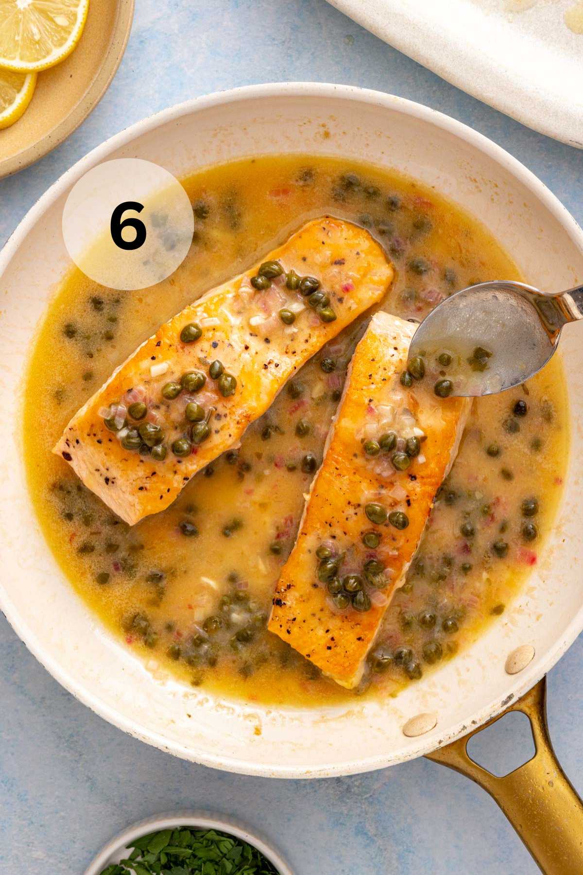 Spooning sauce over salmon fillets in a skillet.
