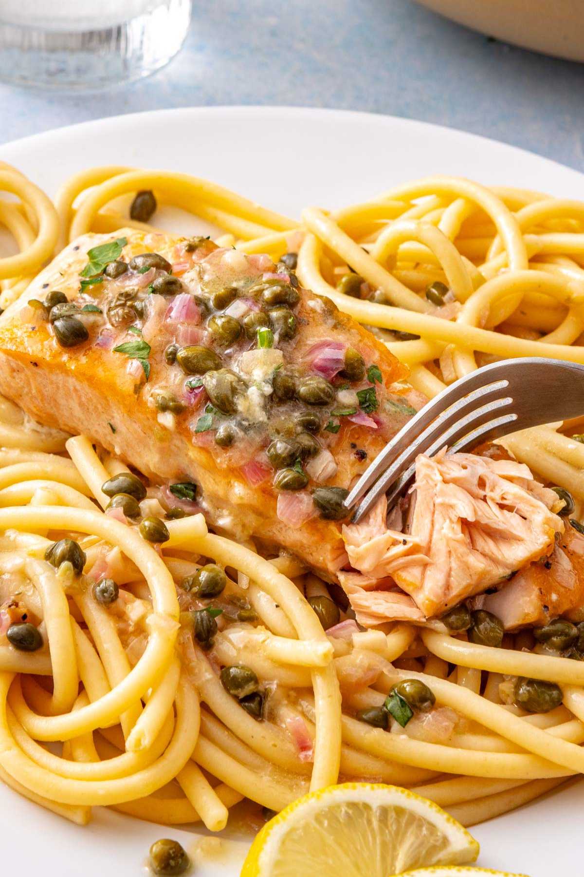 Use a fork to flake salmon that's served over spaghetti.