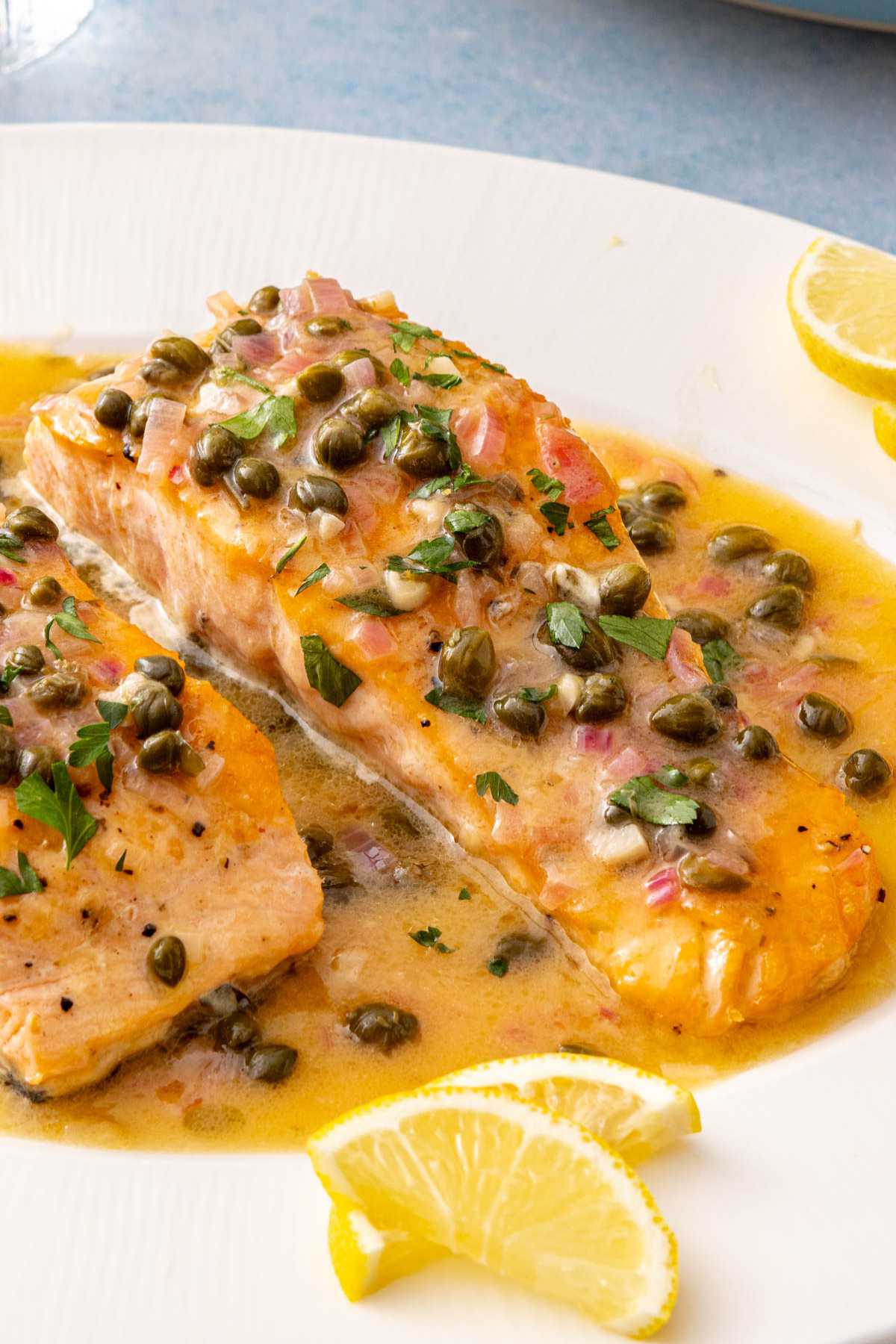 Salmon Piccata on a white plate served with lemon wedges.