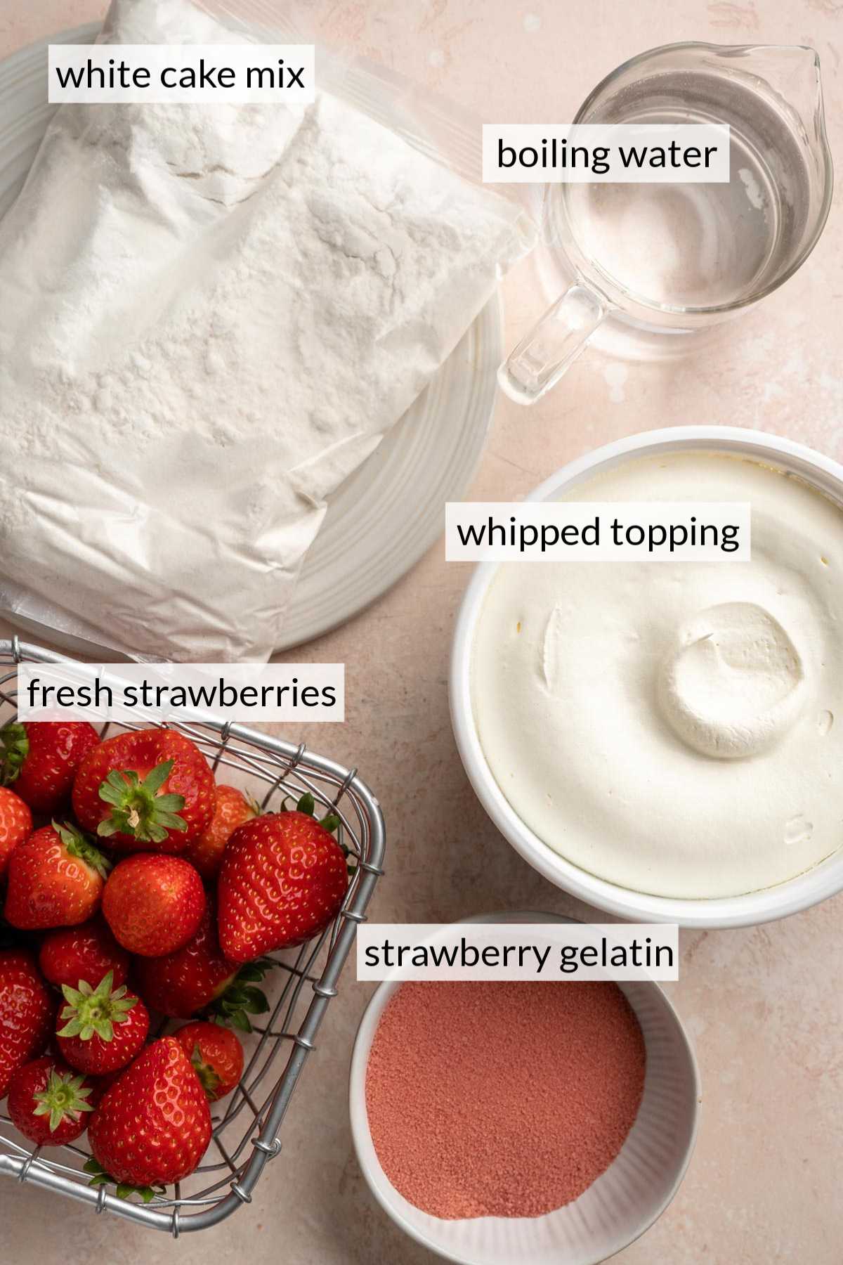 A package of cake mix near a glass of water, a tub of whipped topping, strawberry gelatin and fresh strawberries.