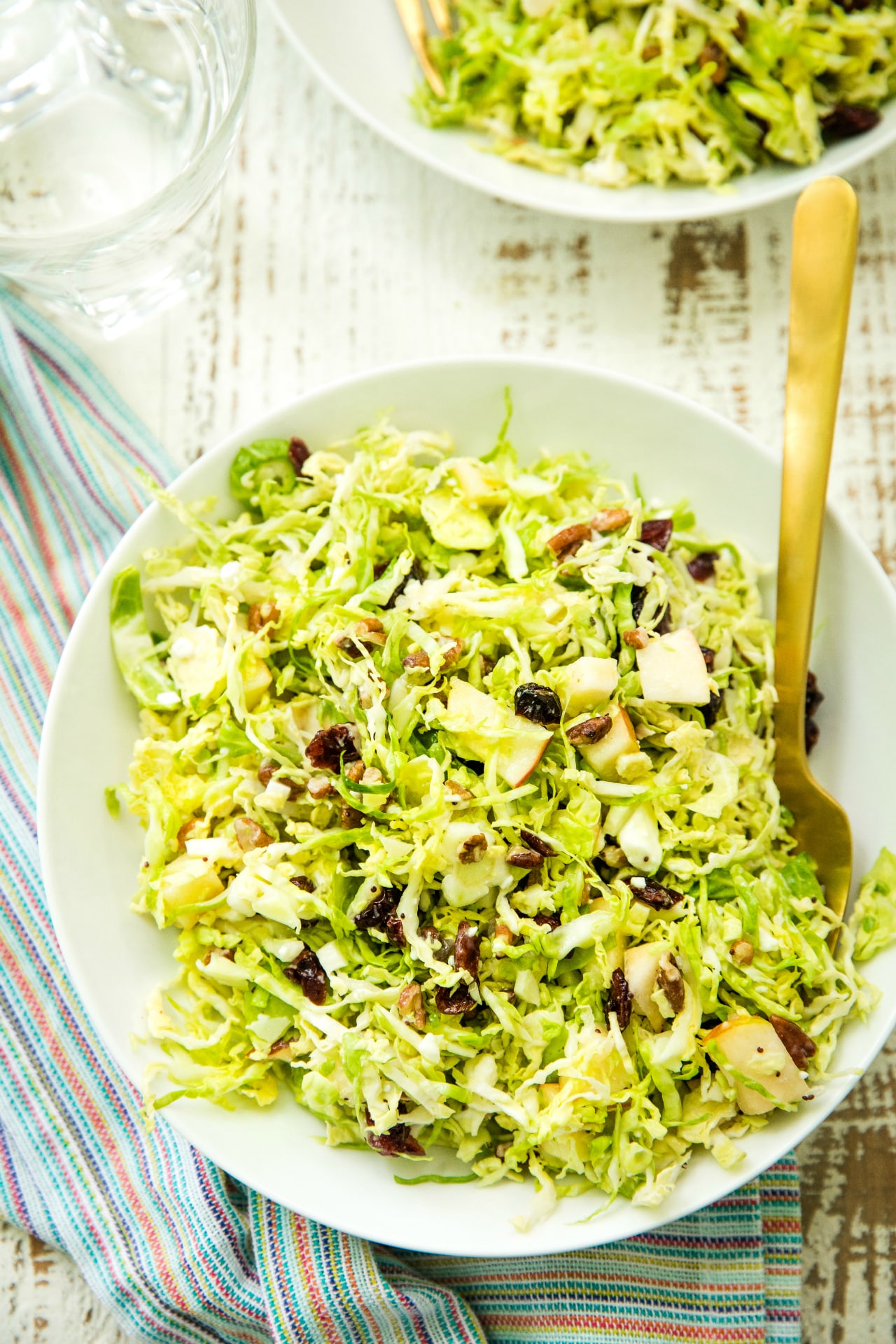 overhead view of a Autumn Shredded Brussels Sprouts Apple Salad in a white bowl with a gold fork