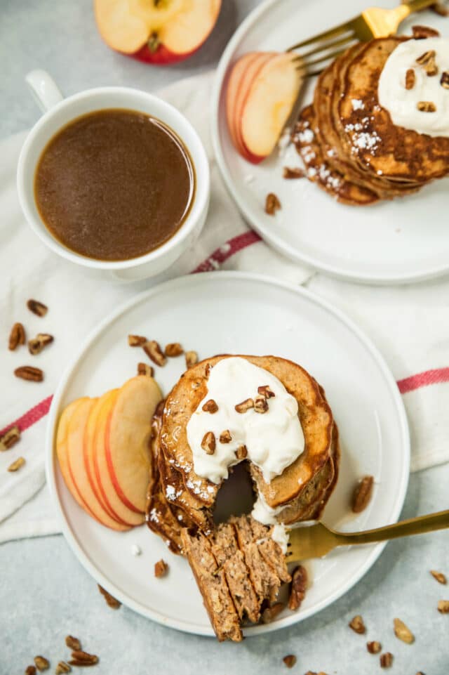 overhead photo of Apple Cinnamon Protein Pancakes on white plates, served with a cup of coffee