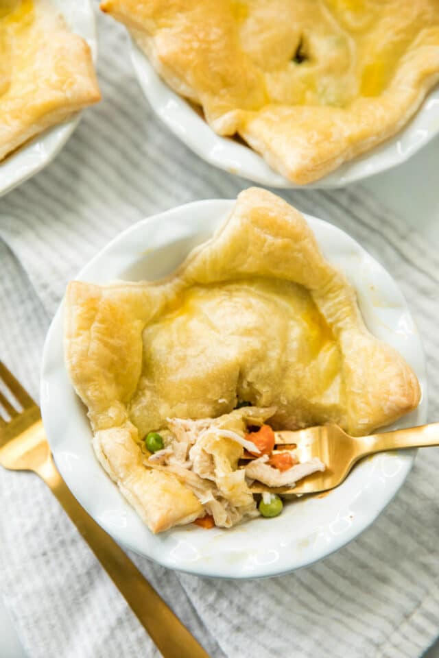 overhead photo of Rotisserie Chicken Pot Pie in a mini white pie plate with a gold fork taking a bite out