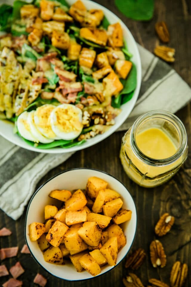 overhead of the Healthy Harvest Cobb Salad served in a white bowl with a dish of cubed butternut squash and a glass jar of dressing
