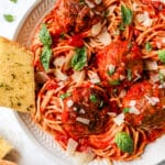spaghetti and meatballs served with garlic and bread and topped with fresh basil