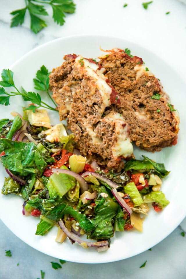 closeup overhead image of slices of Cheesy Italian Meatloaf Recipe on a white plate with a side salad