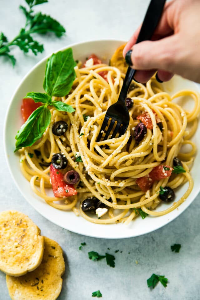 closeup overhead image of Easy Greek Pasta Salad in a white bowl with a woman's hand holding a black fork