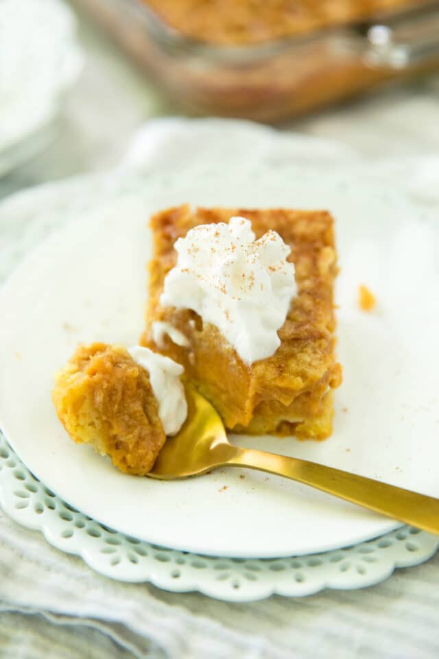 closeup image of Pumpkin Dessert Squares served on a white plate with a gold spoon and topped with whipped cream