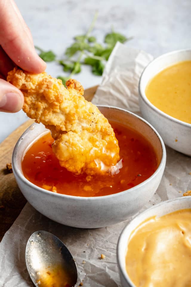 Dipping a chicken tender into a bowl of apricot chili sauce.