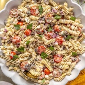 Pasta salad in a large white bowl with tomatoes and a creamy dressing.