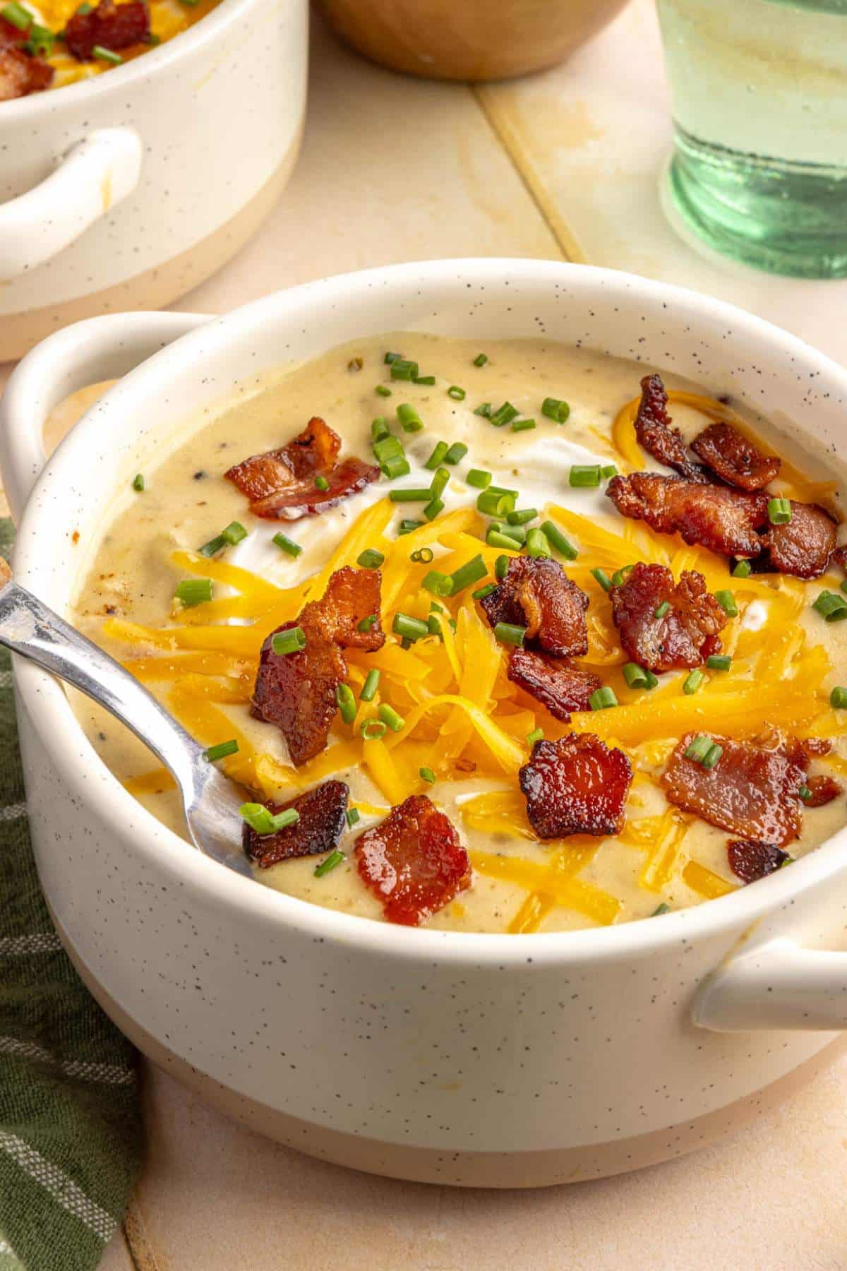 Potato soup in a bowl garnished with cheddar cheese, bacon and chives.