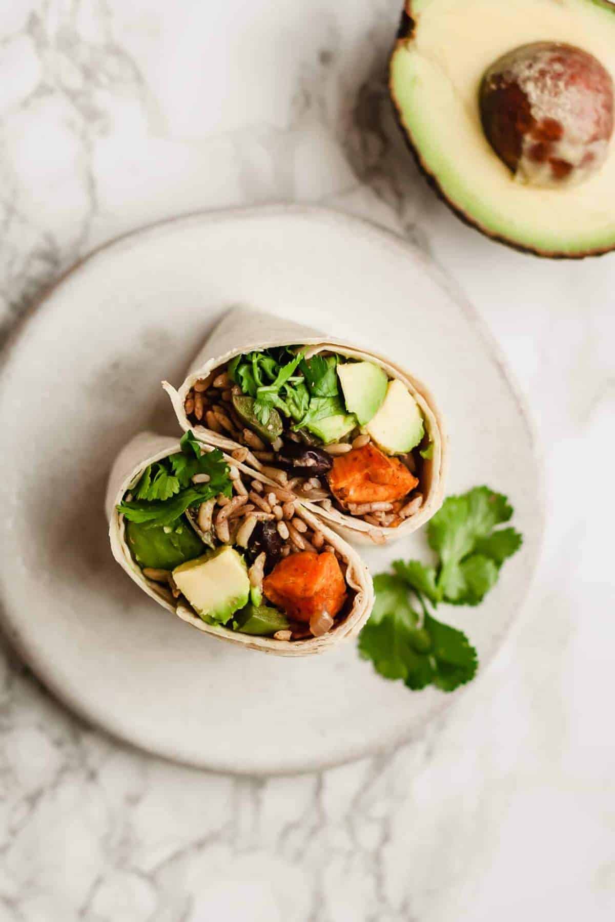 Burrito with sweet potatoes, black beans, avocado and rice sliced in half.