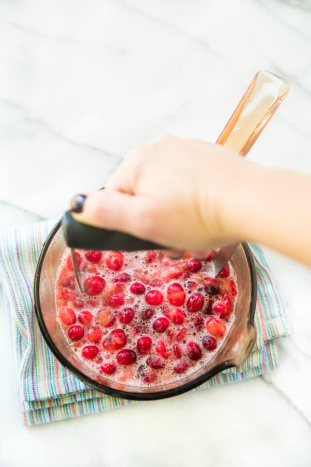 woman's hand mashing cranberries in a saucepan 