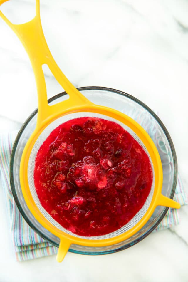 straining cranberry syrup in a glass bowl