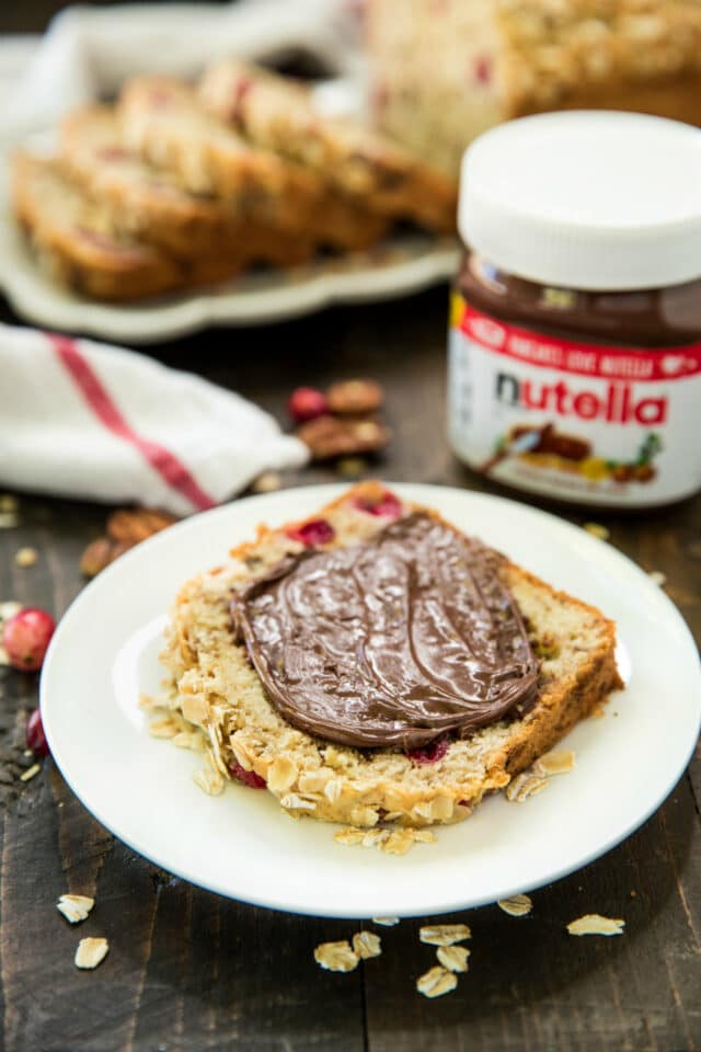 slice of cranberry quick bread on a white plate with a jar of Nutella
