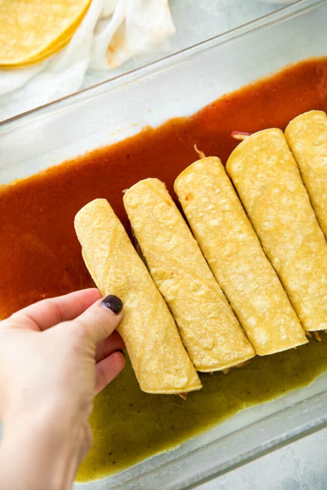 woman's hand placing rolled corn tortillas in a baking dish
