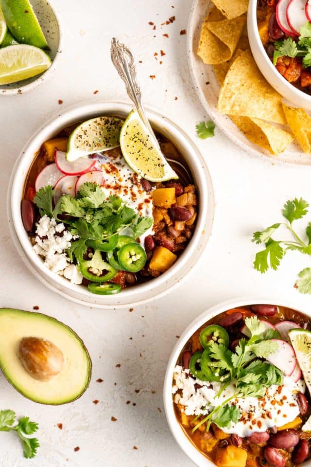 bowls of vegan butternut squash chili served with lime and avocado