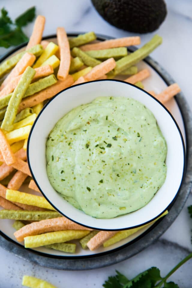 avocado cilantro lime dip in a white bowl served with veggie straw chips on a white plate
