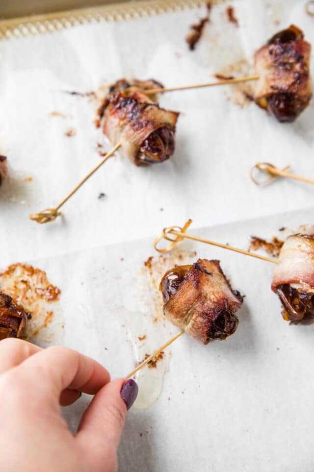 woman's hand turning the bacon wrapped date with the toothpick