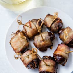 Bacon Wrapped Dates on a white plate served with a glass of white wine