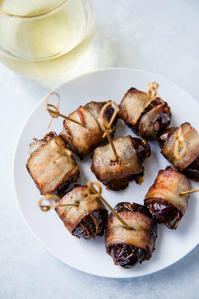 Bacon Wrapped Dates on a white plate served with a glass of white wine