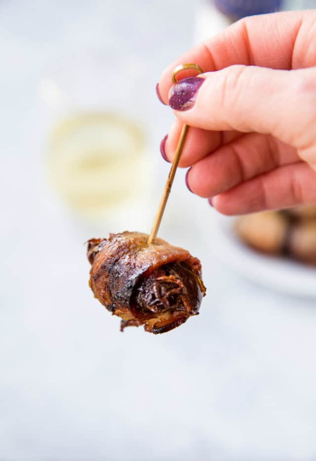 woman's hand holding a toothpick through a bacon wrapped date 