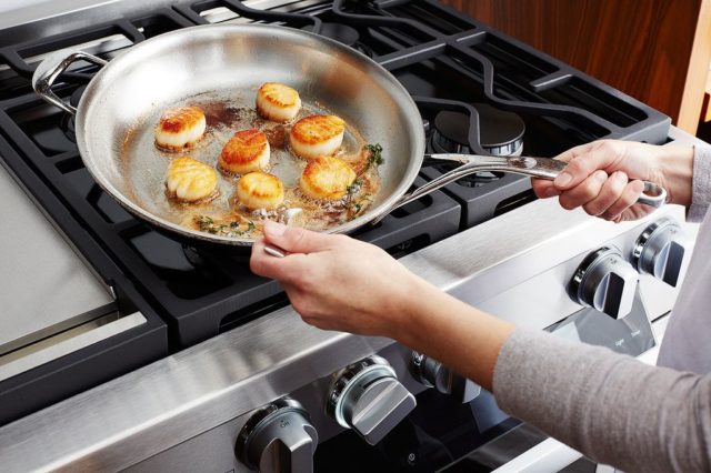 woman's hands using stainless steel skillet to cook scallops