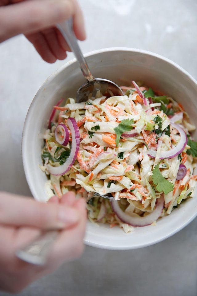 woman's hands using salad spoons to toss coleslaw in a large white bowl