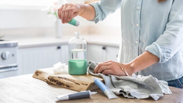 woman in kitchen mixing up cleaning solution in glass bottle
