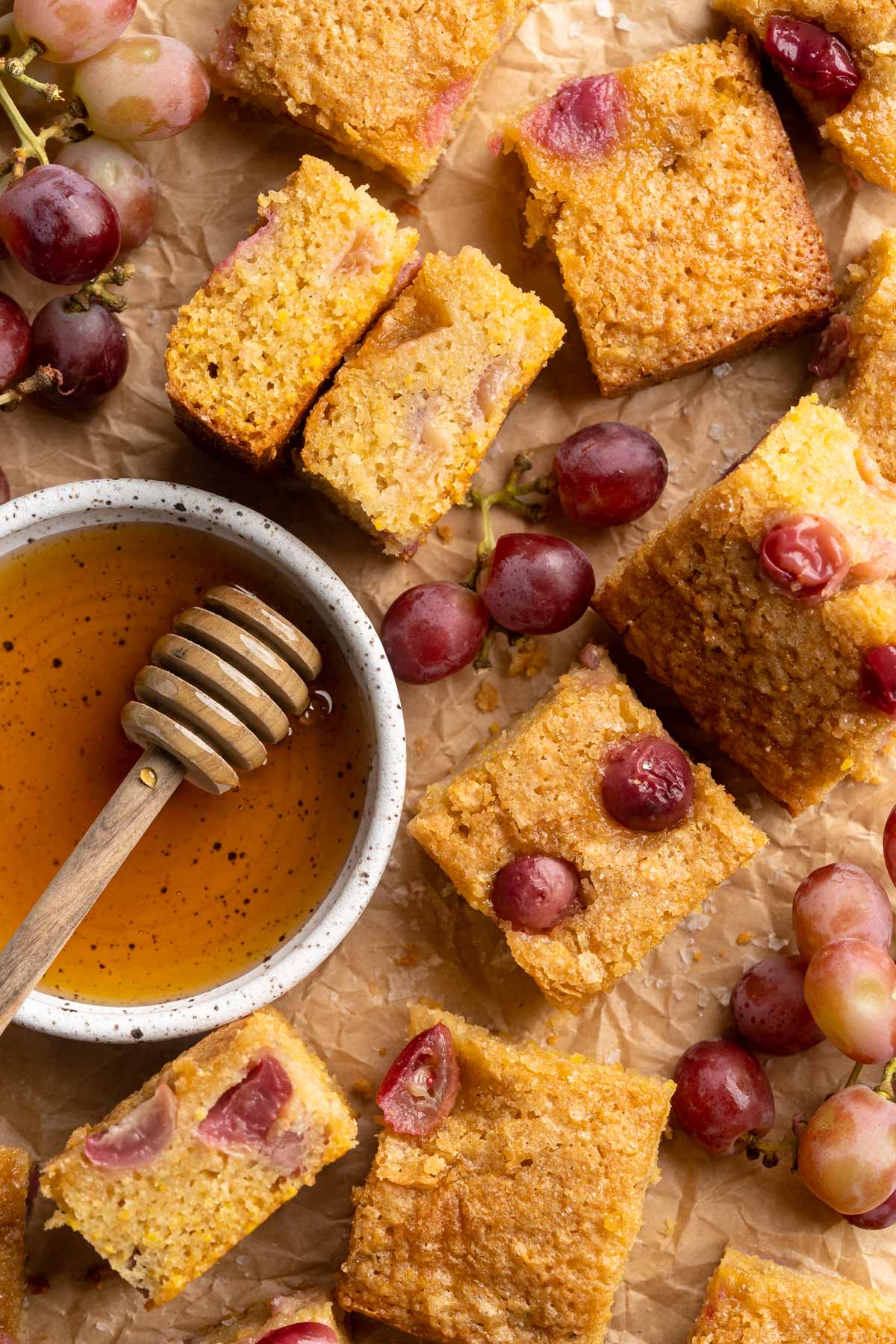 Grape cake squares near a bowl of honey and purple grapes.