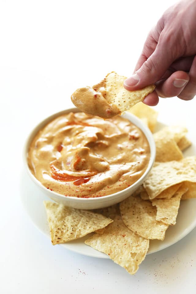 hand dipping tortilla chip in queso dip