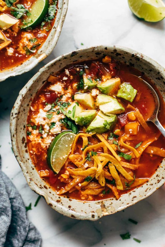 tortilla soup in a spotted bowl with a spoon and topped with avocado, lime and tortilla strips 