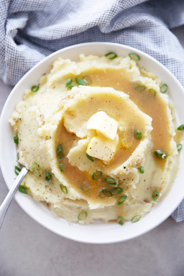 mashed potatoes topped with brown gravy and butter in large white serving bowl