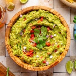 Bowl of guacamole garnished with fresh cilantro, diced tomato and onion.