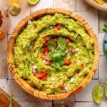 Bowl of guacamole garnished with fresh cilantro, diced tomato and onion.