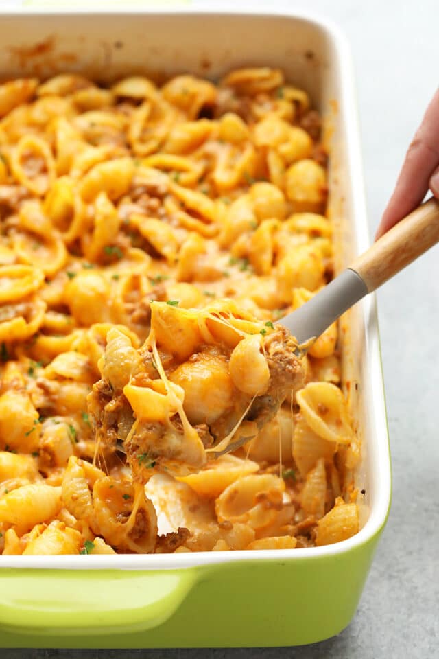 cheesy pasta casserole in a large casserole dish with a serving spoon dishing some out