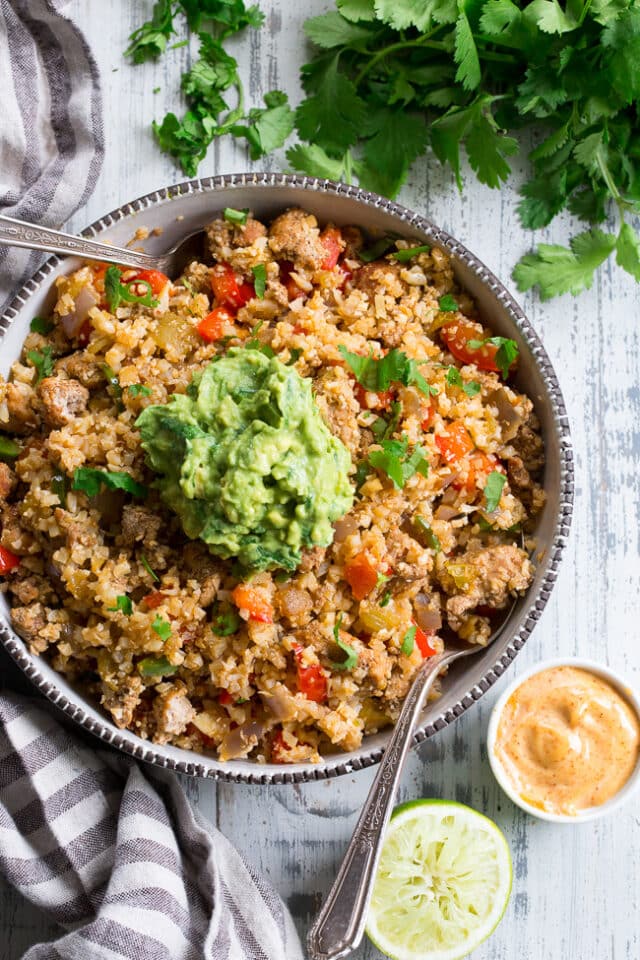 Mexican Cauliflower Fried Rice in a large serving bowl with silver spoons, topped with guacamole 