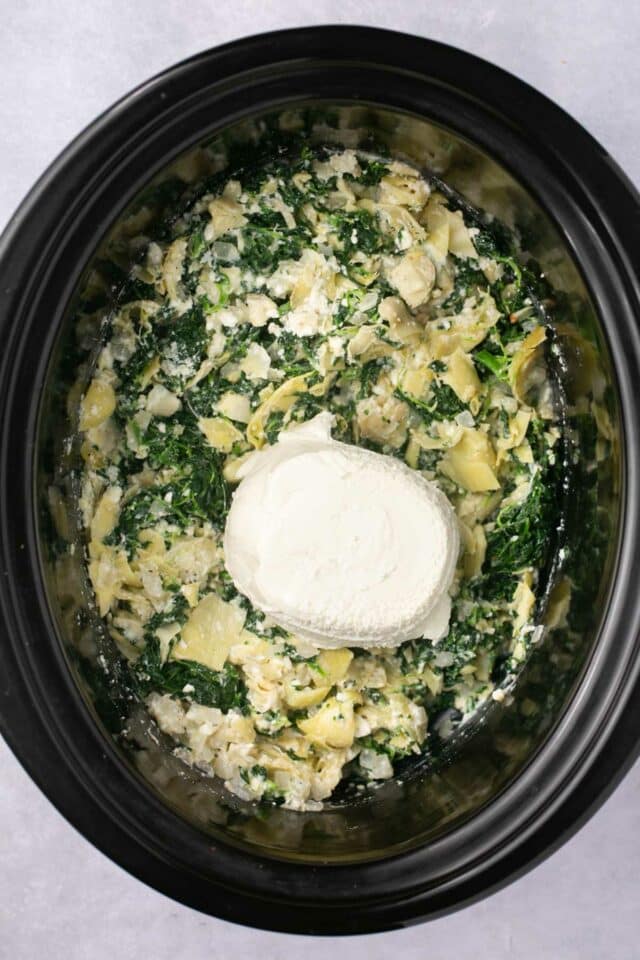 All ingredients add to a crockpot for spinach artichoke dip and cream cheese on top.