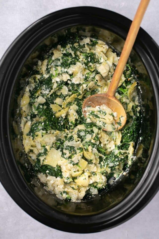 Stirring spinach with artichokes and cheese in a slow cooker.