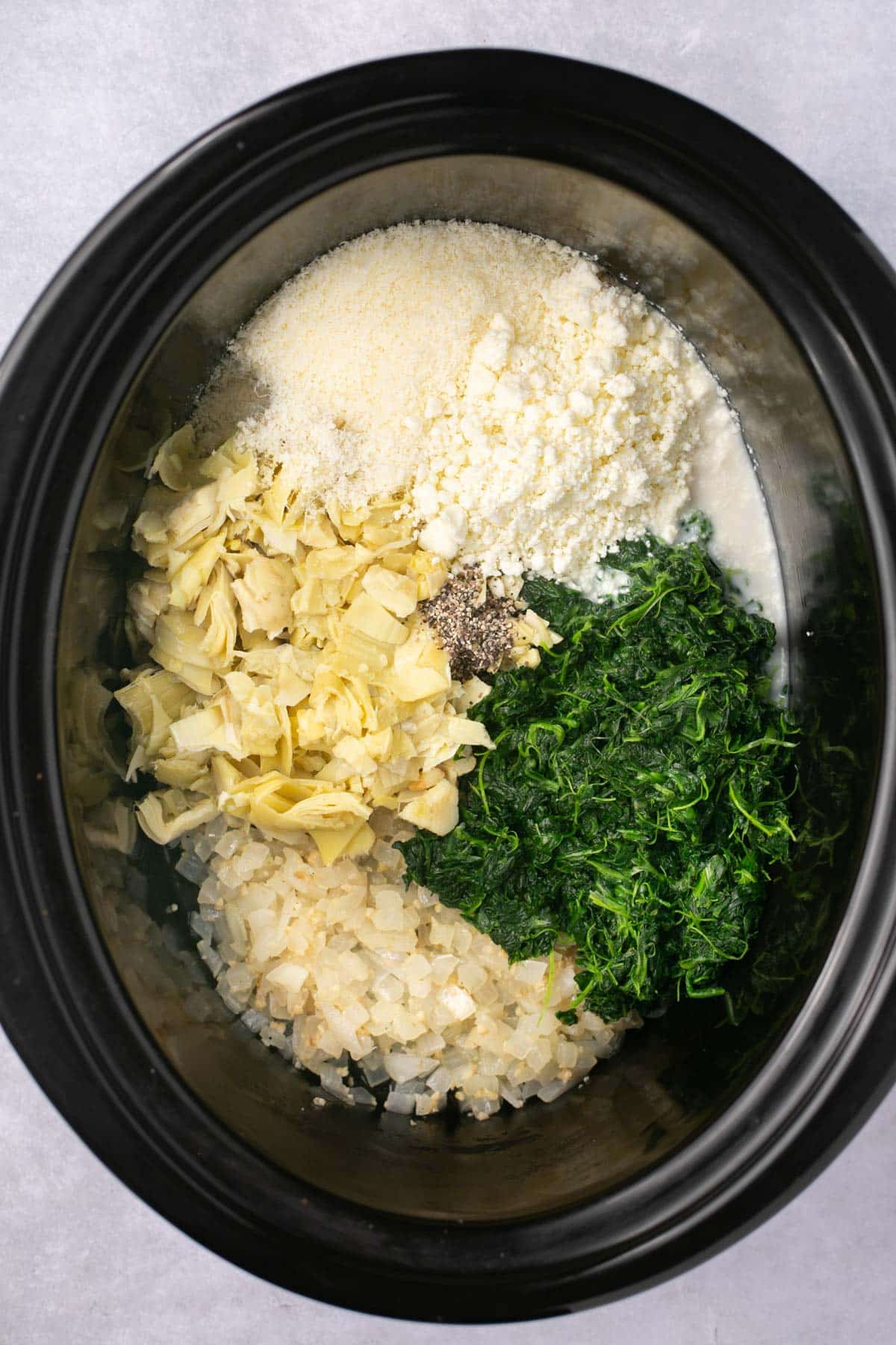 Ingredients for spinach artichoke dip added to a slow cooker.