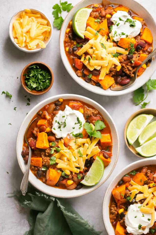 White bowls filled with sweet potato chili and toppings.