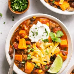A bowl of sweet potato chili topped with shredded cheese, sour cream and a lime wedge.