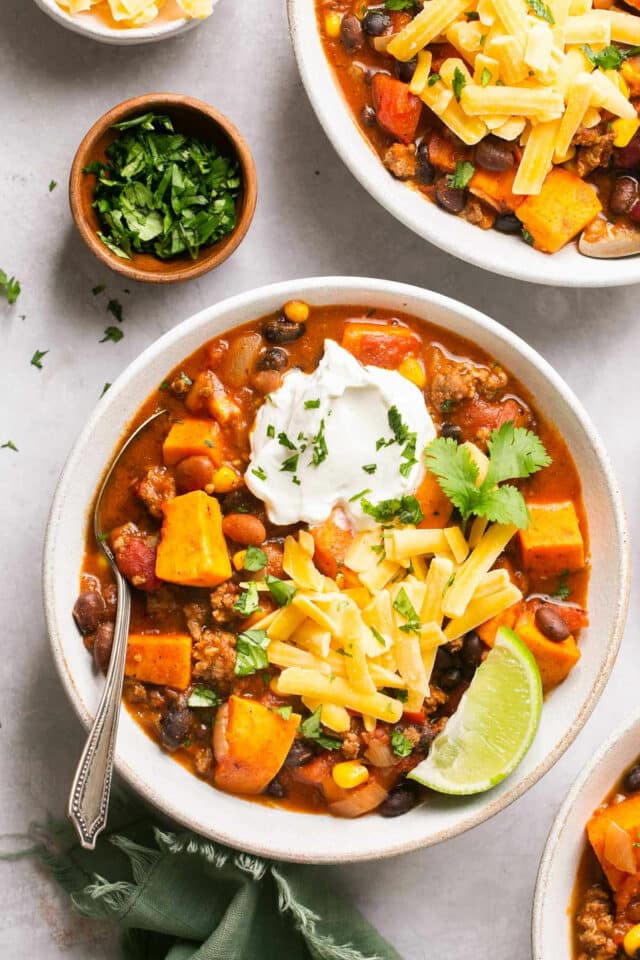 A bowl of sweet potato chili topped with shredded cheese, sour cream and a lime wedge.
