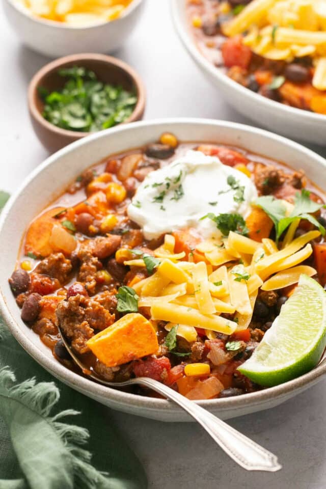 Sweet potato chili topped with shredded cheese, cilantro and sour cream in a white bowl.