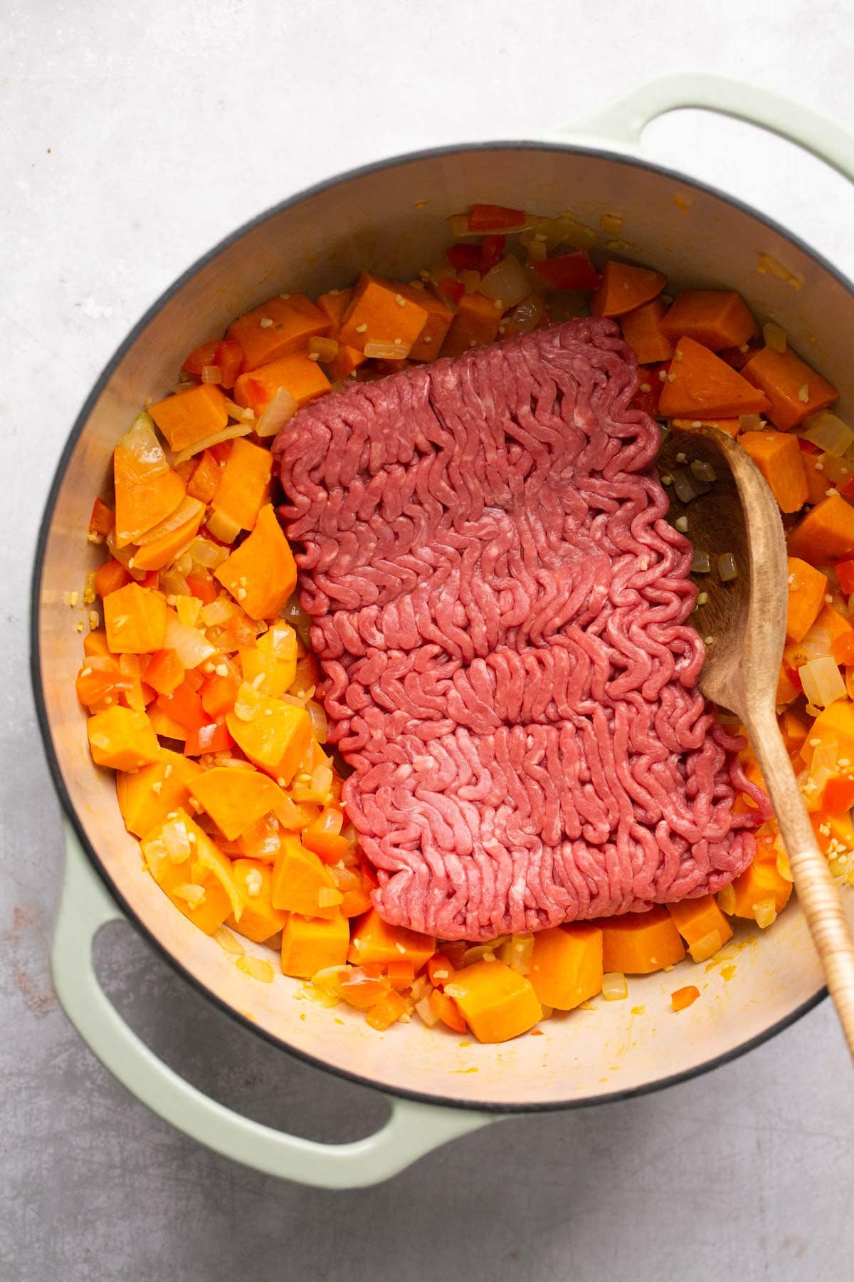 Adding ground beef to cooking vegetables.